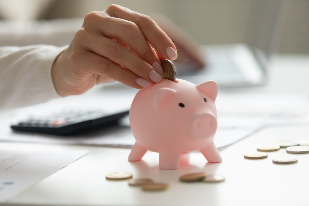 Close,Up,Woman,Holding,Smartphone,,Putting,Coin,In,Pink,Piggy